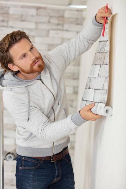 young man installing wallpaper at home - Fotó, kép