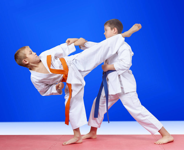 Хлопці тренують удари рукою і ногою на синьому фоні
 - Фото, зображення