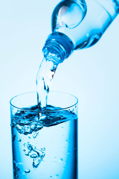 Water uit een fles in glas gieten op een blauwe achtergrond. Kopieerruimte. - Foto, afbeelding