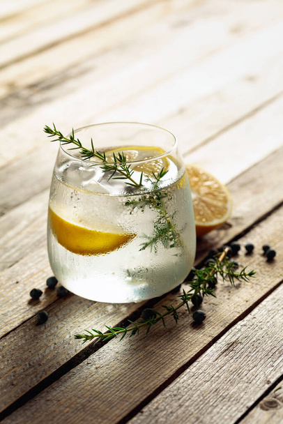 Bebida alcohólica (cóctel gin tonic) con limón, rama de enebro y hielo en una mesa de madera rústica, espacio para copiar. Bebida de cóctel helado con limón y bayas de enebro. - Foto, imagen