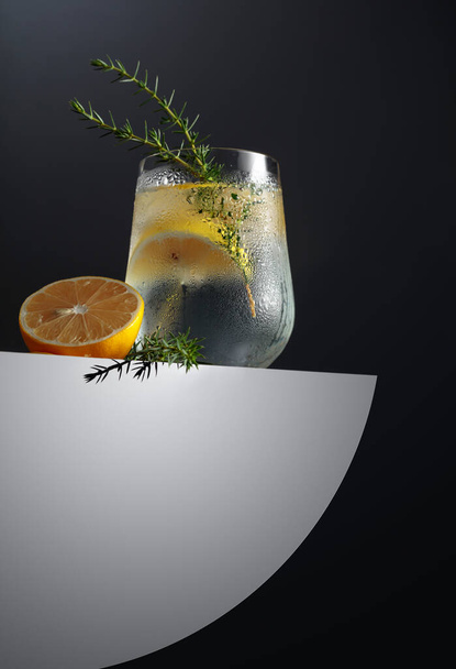 Алкогольный напиток (джин-тоник) с лимоном, можжевеловой веткой и льдом на тёмном фоне, копировальное место. Коктейль с лимоном.  - Фото, изображение
