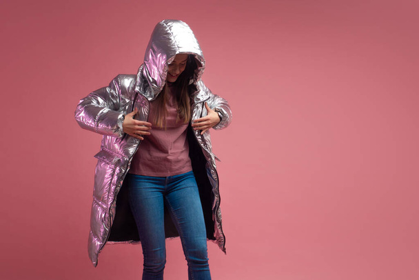 fashionable and modern young woman in a puffy light down jacket throws a hood over her head. - Foto, Bild