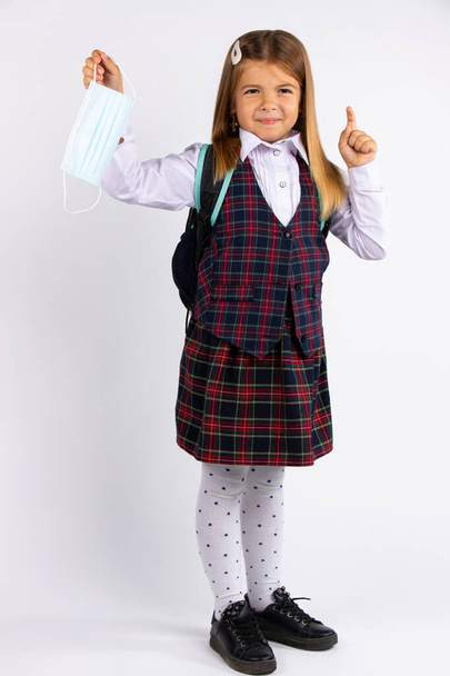 Opleiding tijdens quarantaine covid. Kind meisje in uniform wijst vinger naar de zijkant, geïsoleerd op grijze achtergrond. - Foto, afbeelding
