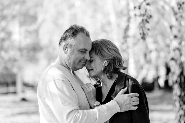 Мужчина средних лет и женщина с headphones.a мужчина нежно обнимает свою жену. Черное белое фото - Фото, изображение