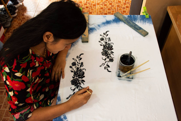 Тайская народная художница изобразила узор с натуральным цветом индиго на платке на столе в мастерской при доме в Нонтхабаде, Таиланд - Фото, изображение