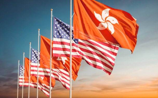 Σημαίες Χονγκ Κονγκ και ΗΠΑ κυματίζουν στο θολό φόντο του ουρανού. Έννοια των διεθνών σχέσεων του Χονγκ Κονγκ. - Φωτογραφία, εικόνα