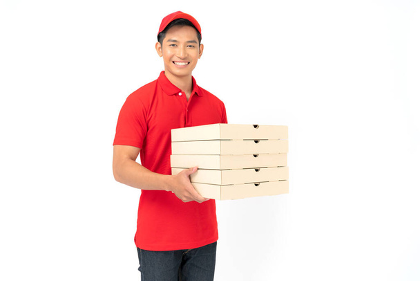Mosolygós futár alkalmazott piros sapkás üres póló egyenruha áll, amely élelmiszer rendelés és gazdaság pizza dobozok elszigetelt fehér háttér - Fotó, kép