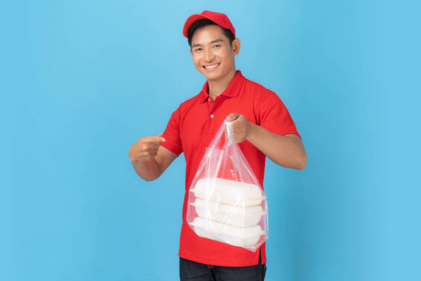 Χαμογελαστός υπάλληλος delivery σε κόκκινο καπέλο λευκό πουκάμισο ομοιόμορφη στέκεται με δίνοντας παραγγελία τροφίμων που απομονώνονται σε μπλε φόντο - Φωτογραφία, εικόνα