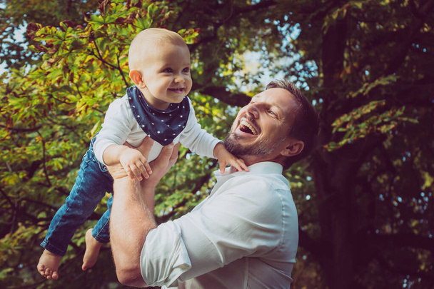 Привлекательный отец держит милого улыбающегося ребенка в лесу - Фото, изображение