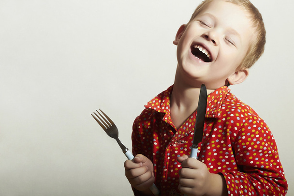 grappige kleine knappe jongen met mes en vork. hongerig kind. glimlachend kind. willen eten - Foto, afbeelding
