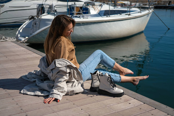 Egy fehér cipős lány ül a mólón egy jachtklubban, újságot olvas és pihen. új lábbeli kollekció ősz tél 20 / 21 divat fotó Lubeck, Németország szeptember 2020 - Fotó, kép