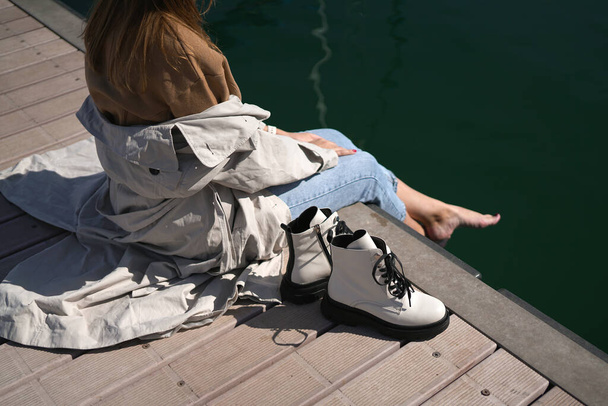 una ragazza con le scarpe bianche si siede su un molo in uno yacht club, legge un giornale e si riposa. nuova collezione di calzature autunno inverno 20 / 21 foto di moda Lubecca, Germania settembre 2020 - Foto, immagini