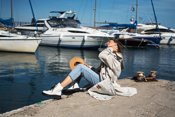 дівчина в білих черевиках сидить на пірсі в яхт-клубі, читає газету і відпочиває. Нова колекція взуття осінню зиму 20 / 21 fashion photo Lubeck, Germany september 2020 - Фото, зображення
