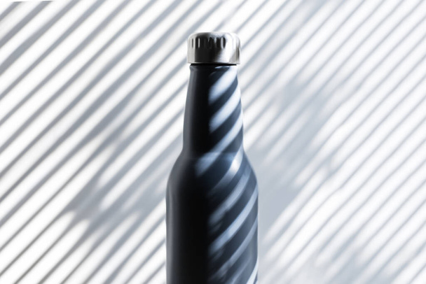 Acél közelkép, öko-újrahasznosítható termo-vizes palack árnyékban, vonalak formájában. - Fotó, kép