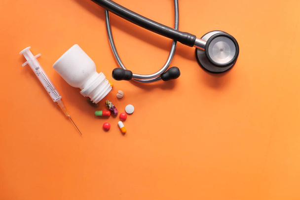 плоский состав стетоскопа, шприца и таблеток на оранжевом фоне  - Фото, изображение