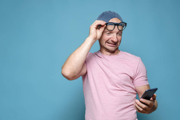 Divertido hombre levantó las gafas a la frente y lee un mensaje en un teléfono inteligente, con una expresión extraña en la cara. Copiar espacio.  - Foto, imagen