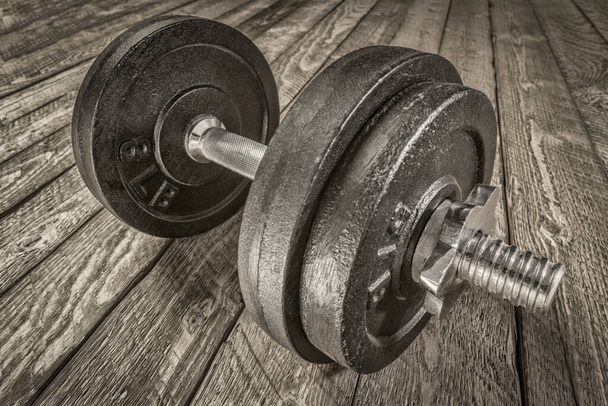 iron dumbbell on a grunge wooden deck - fitness concept, black and white image - Foto, imagen