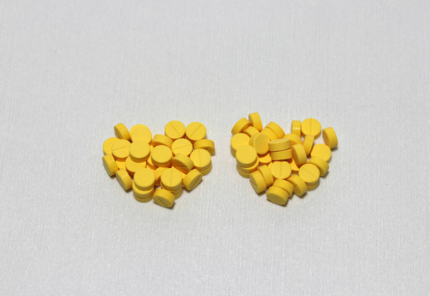 Un par de pilas de medicina amarilla redonda puestas en forma de corazón en el suelo blanco. El concepto de enamorados en el hospital o día de San Valentín. - Foto, imagen