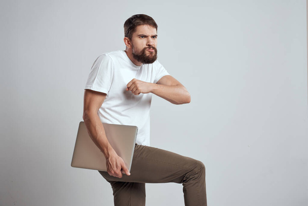 Ein Mann mit einem Laptop in der Hand auf hellem Hintergrund in einem weißen T-Shirt Emotionen Licht Hintergrund neue Technologien - Foto, Bild
