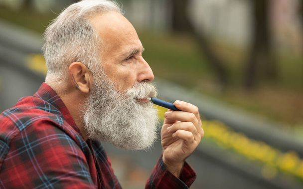 Senior man with beard breathe out smoke. Smoking electronic cigarette. Stress relief concept. Smoking device. Man long beard relaxed with smoking habit. Bearded man vaping. IQOS. - 写真・画像
