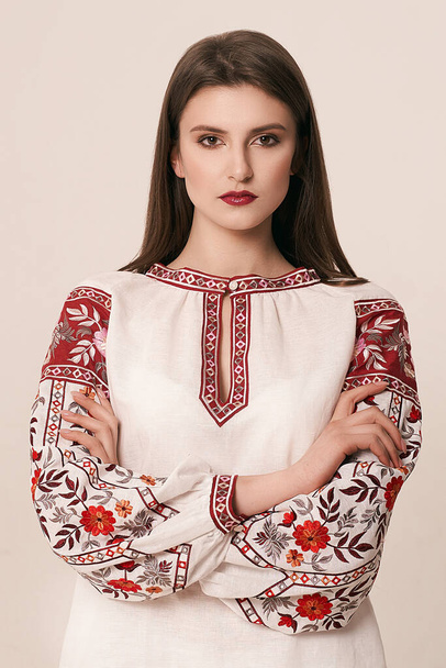 Young beautiful brunette girl wearing gorgeous ethnic style embroidered shirt, modern derivative from traditional Ukrainian vyshyvanka design. Fashion model in studio. - Photo, image