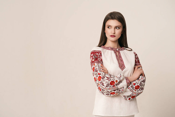 Young beautiful brunette girl wearing gorgeous ethnic style embroidered shirt, modern derivative from traditional Ukrainian vyshyvanka design. Fashion model in studio. - Фото, изображение