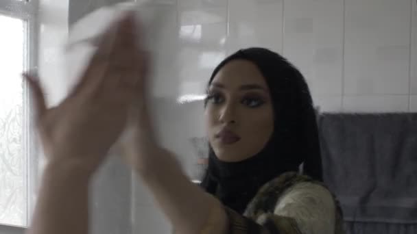Молодая мусульманка стирает зеркало ванной с помощью ткани. Потерянные - Кадры, видео
