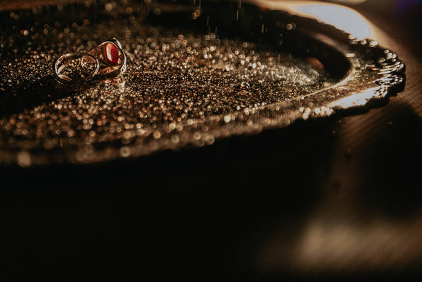 два кольца лежат на металлическом подносе с маленькими капельками воды, также капли воды сверху; вид сбоку - Фото, изображение