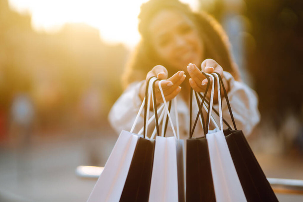 Close up of a woman's hand hold out black and white shopping bags. Young woman with packages after shopping at sunset. Purchases, black friday, discounts, sale concept. - Foto, immagini