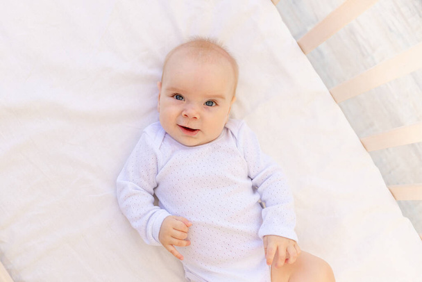 portrait d'une petite fille de 6 mois en body blanc couchée sur le dos sur un lit blanc, espace pour le texte - Photo, image