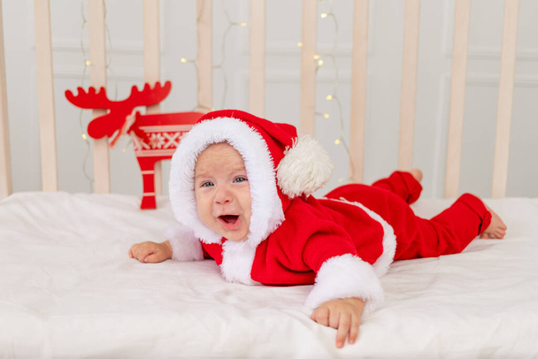 a small child is lying in a Santa costume in the crib and crying - Photo, Image
