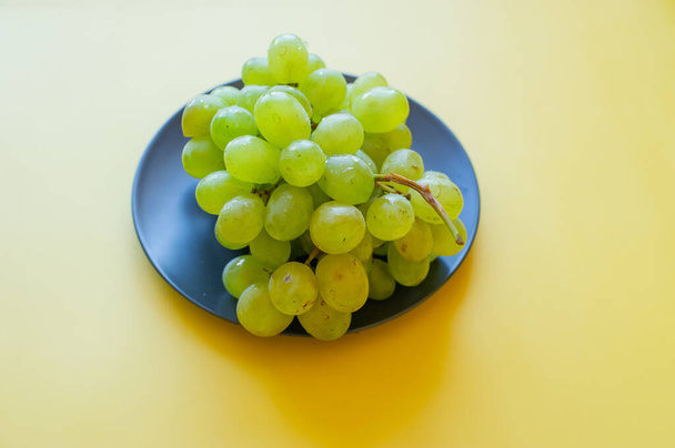 Green grapes in a black plate. Grapes on a yellow background. vitamin - Valokuva, kuva