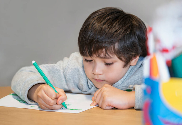 Portré iskolás gyerek ül egyedül csinál házi feladatot, Gyermek fiú kezében fekete toll rajz és írás fehér papírra az asztalon, Általános iskola és magániskola koncepció - Fotó, kép
