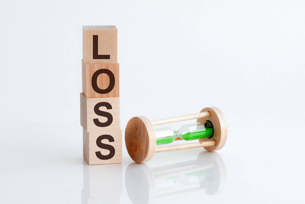 zandloper en houten blokken met het woord LOSS. Het concept van financieel verlies. Investeren in een zakelijk project. De juiste beslissing nemen. Onroerend goed verzekering. Juridisch marktverlies - Foto, afbeelding