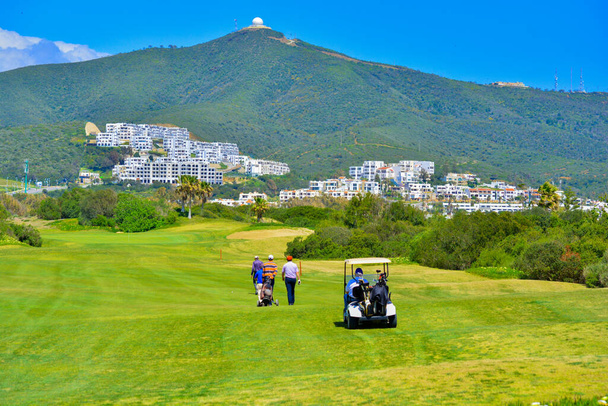 Golf cart su un campo da golf. Campo verde e cielo azzurro nuvoloso. Paesaggio primaverile con erba e alberi - Foto, immagini