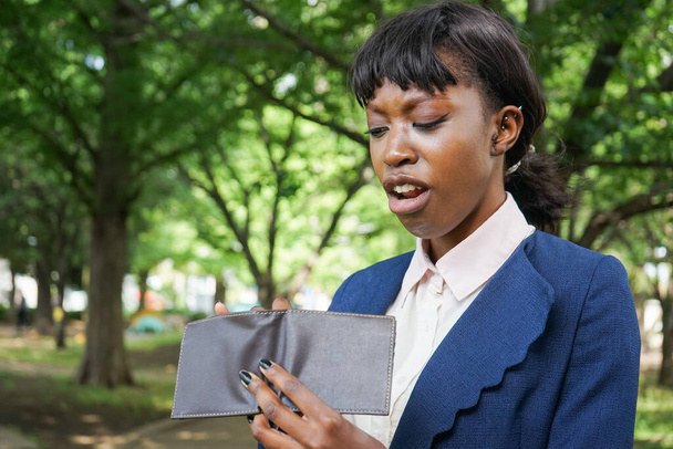 Αφρικανή γυναίκα κοιτάζει το πορτοφόλι της σε εξωτερικό χώρο - Φωτογραφία, εικόνα