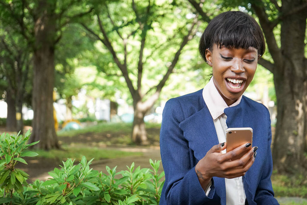 mulher africana usando um smartphone enquanto caminha ao ar livre - Foto, Imagem