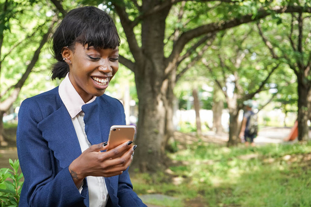 mujer africana usando un teléfono inteligente mientras camina al aire libre - Foto, Imagen