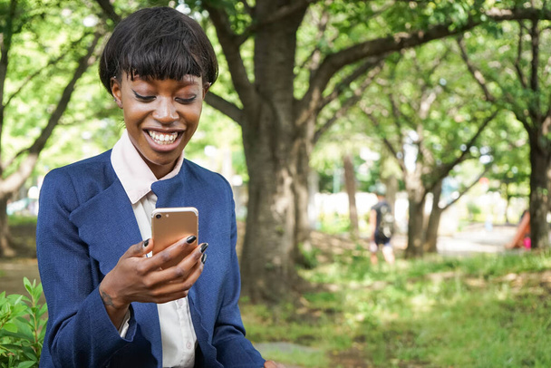屋外を歩きながらスマートフォンを使うアフリカ人女性 - 写真・画像