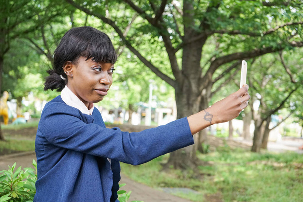 afrikkalainen nainen käyttää älypuhelinta kävellessään ulkona - Valokuva, kuva