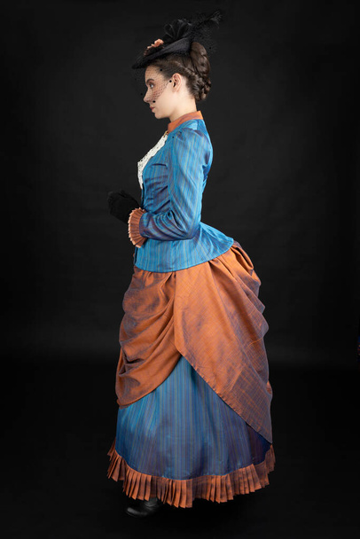 A young Victorian woman in an 1880s ensemble against a black studio backdrop - Fotó, kép