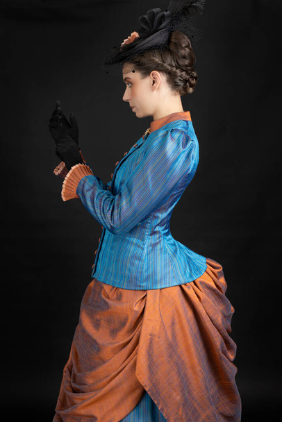 Nuori viktoriaaninen nainen 1880-luvun yhtyeessä mustassa studiossa. - Valokuva, kuva