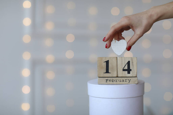Valentine's day concept. Date 14 February on wooden cube calendar on a white gift box and white heart in hand. Bokeh golden and white background. - 写真・画像