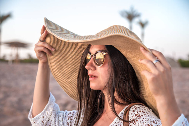 Portré egy elegáns nő egy kalap és szemüveg naplementekor a strandon. Közelről. - Fotó, kép