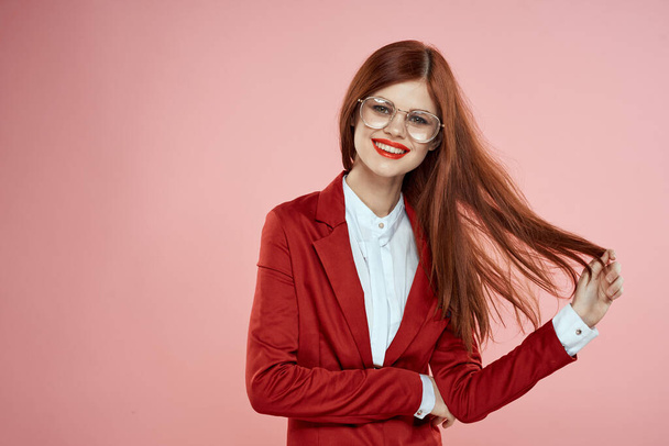 Nainen punaisessa takissa lasit punaiset huulet pitkät hiukset vaaleanpunainen tausta - Valokuva, kuva
