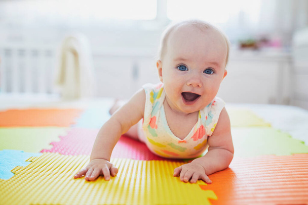 Adorable baby girl doing tummy time on colorful play mat. Happy healthy kid playing on the floor - Foto, Bild