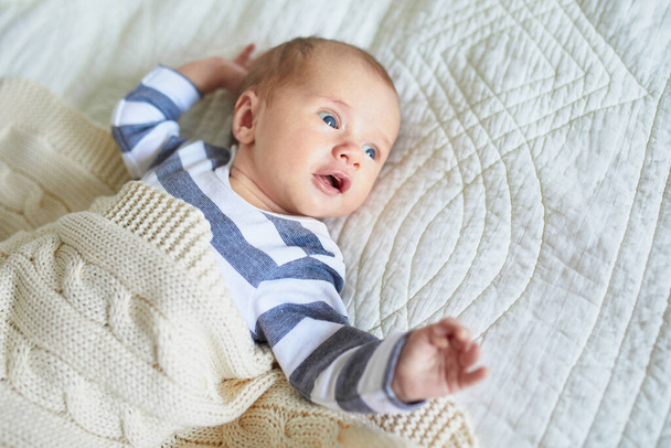 One month baby girl lying under knitted blanket in bedroom - Fotó, kép