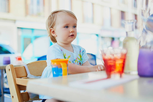 Adorable toddler girl sitting in high chair in cafe or restaurant. Going out with kids concept - Foto, afbeelding