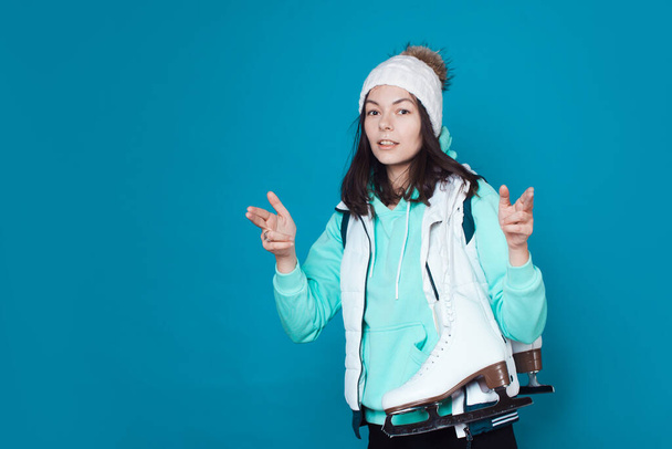 Winter hobby, ice skating. A brunette girl in a hoodie with figure skating skates on her shoulder. - 写真・画像