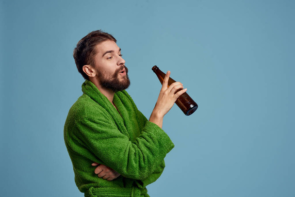 drunk man in a green robe with a bottle of beer in his hand on a blue background alcohol - Photo, Image